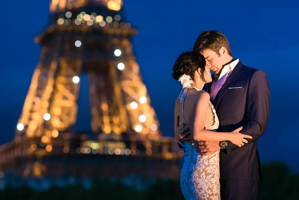 Pre-wedding photos at Bir Hakeim Bridge with couple kissing on wall and illuminated Eiffel Tower backdrop at night