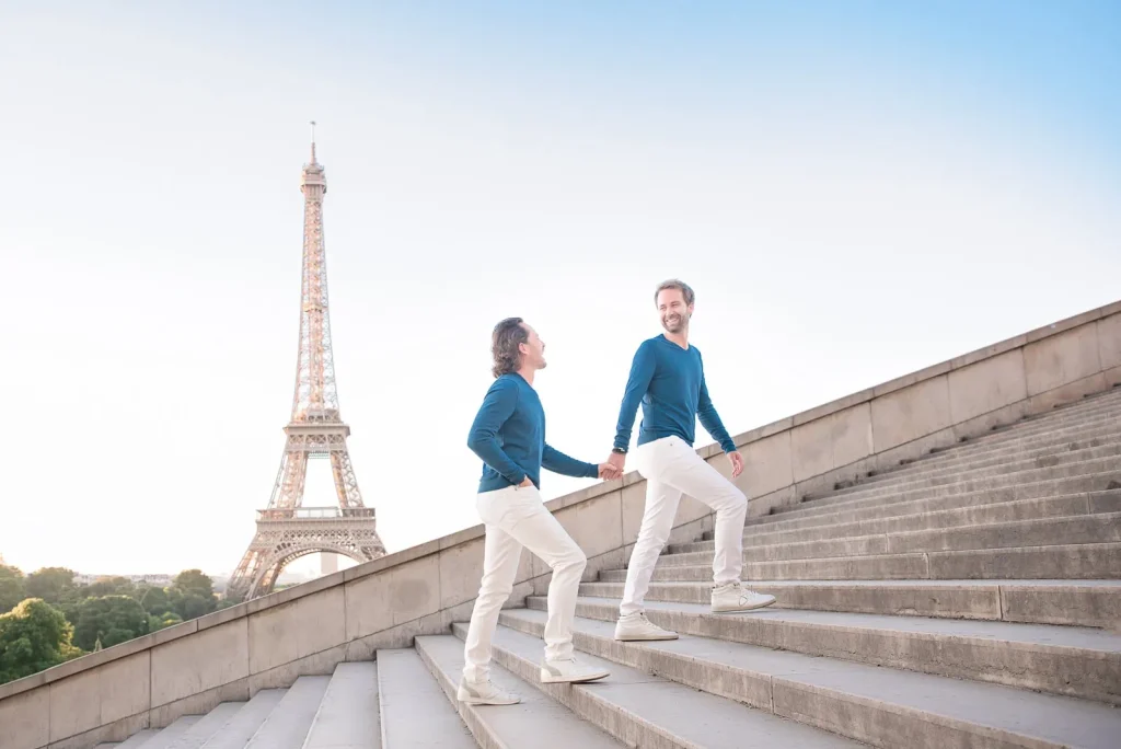 Same-sex couple walking up Trocadero stairs during sunrise engagement session with Eiffel Tower in background, Paris