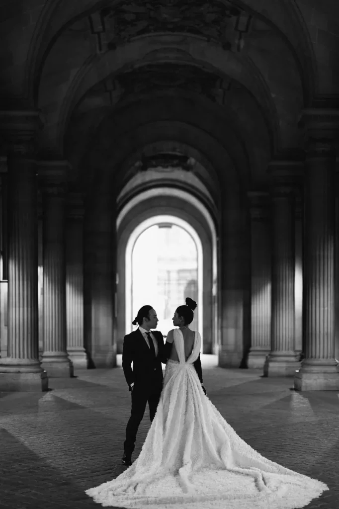 Bride in massive white wedding dress at Louvre underpass architecture after intimate elopement ceremony, black and white Paris photographer