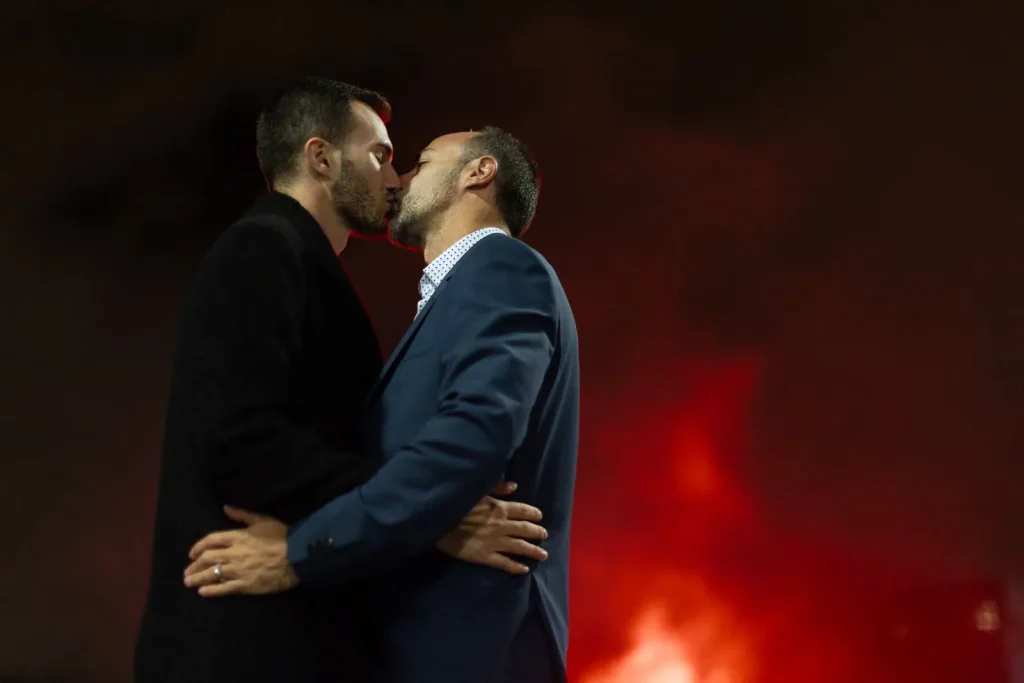 Same-sex couple in tuxedos holding hands walking Bir Hakeim Bridge during golden hour, Paris LGBTQ wedding photographer