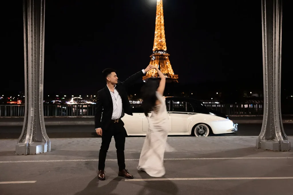 Couple twirling at Bir Hakeim Bridge night with white vintage Rolls Royce convertible and illuminated Eiffel Tower, luxury Paris photographer