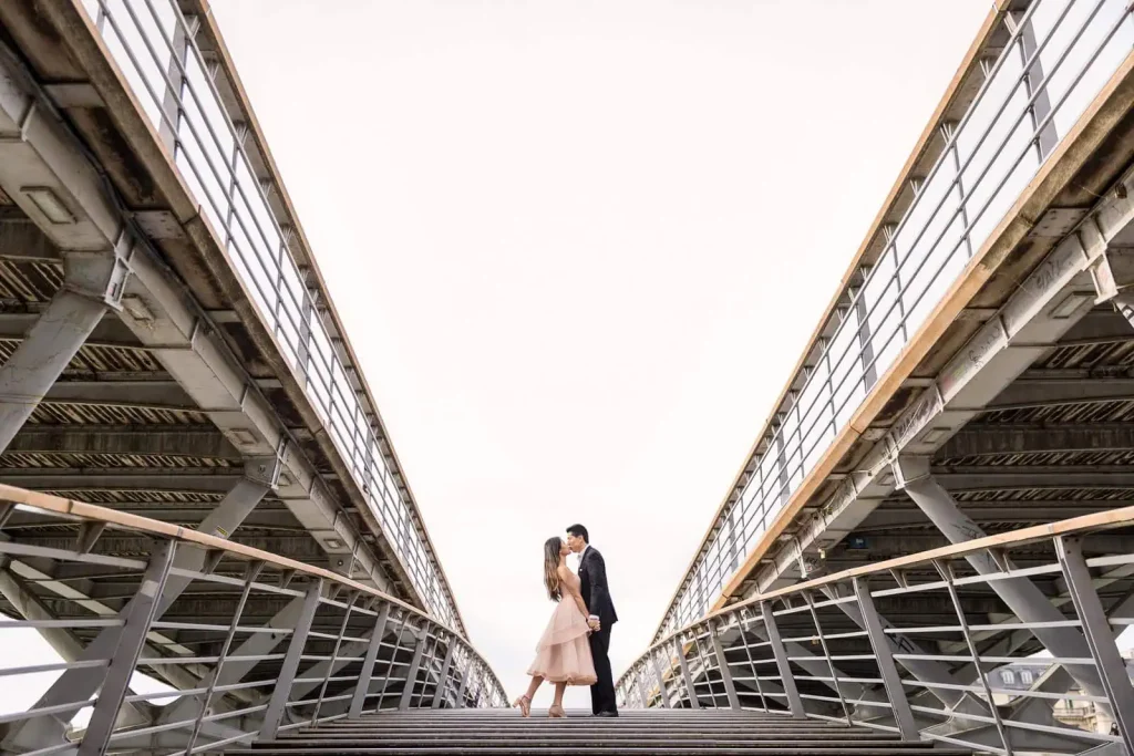 Couple kissing on Passerelle Léopold-Sédar-Senghor bridge during golden hour, artistic Paris engagement photographer session