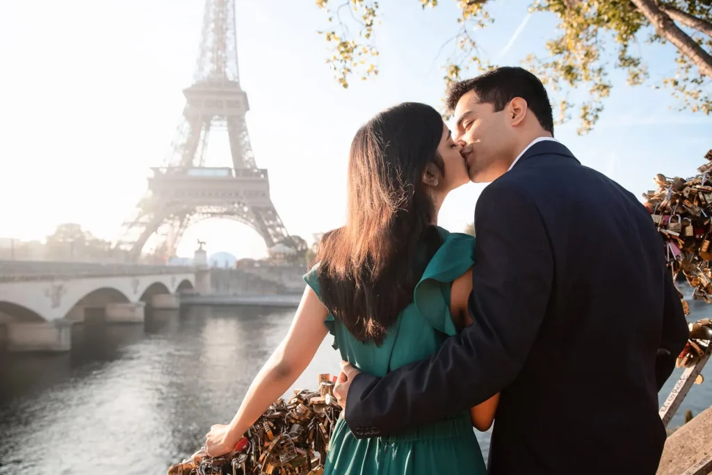 Indian couple kissing softly at Pont d'Iéna Seine riverbank during golden hour with Eiffel Tower view, Paris photographer