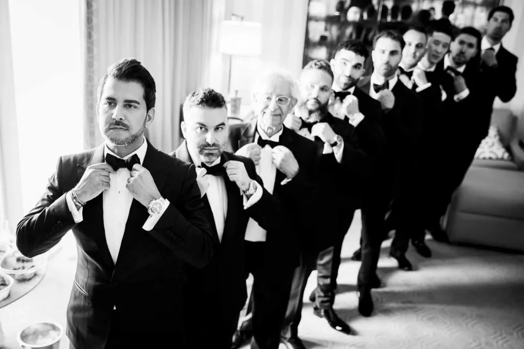 Groom with groomsmen and father in tuxedos adjusting bow ties simultaneously, Paris wedding photographer group portrait