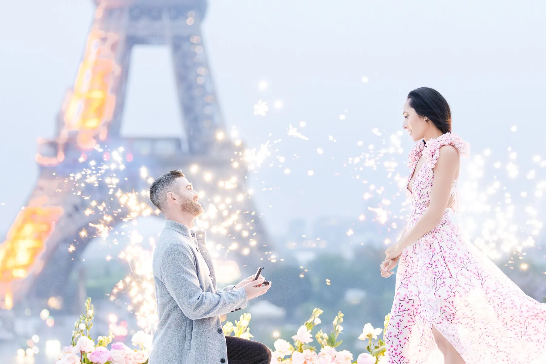 Sunrise Eiffel Tower proposal at Trocadero with man on one knee, pink gown, diamond ring, white floral arrangements, fireworks fountains, and candlelight.