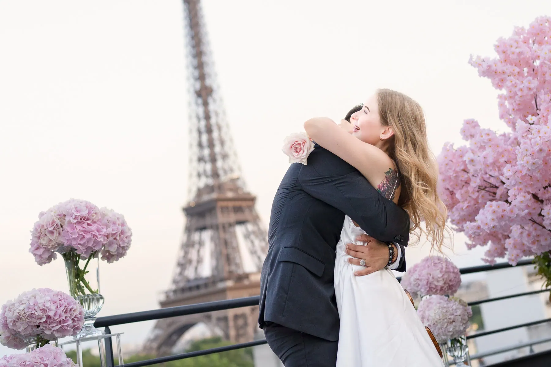 Paris proposal at Shangri La hotel terrace with Eiffel Tower view, couple embracing, pink rose, cherry blossom trees, and pink hydrangea arrangements.